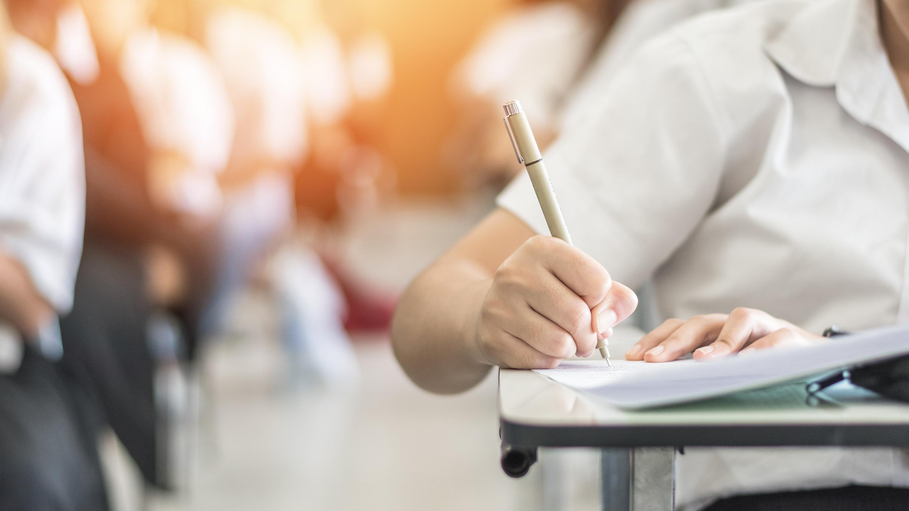 Närbild på en hand som håller i en penna och skriver i ett block i en utbildningssal