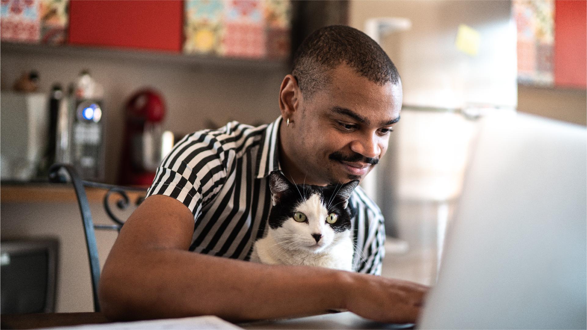 En man sitter vid datorn med sin katt