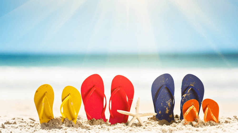 Fyra olikfärgade par sandaler på en sandstrand.