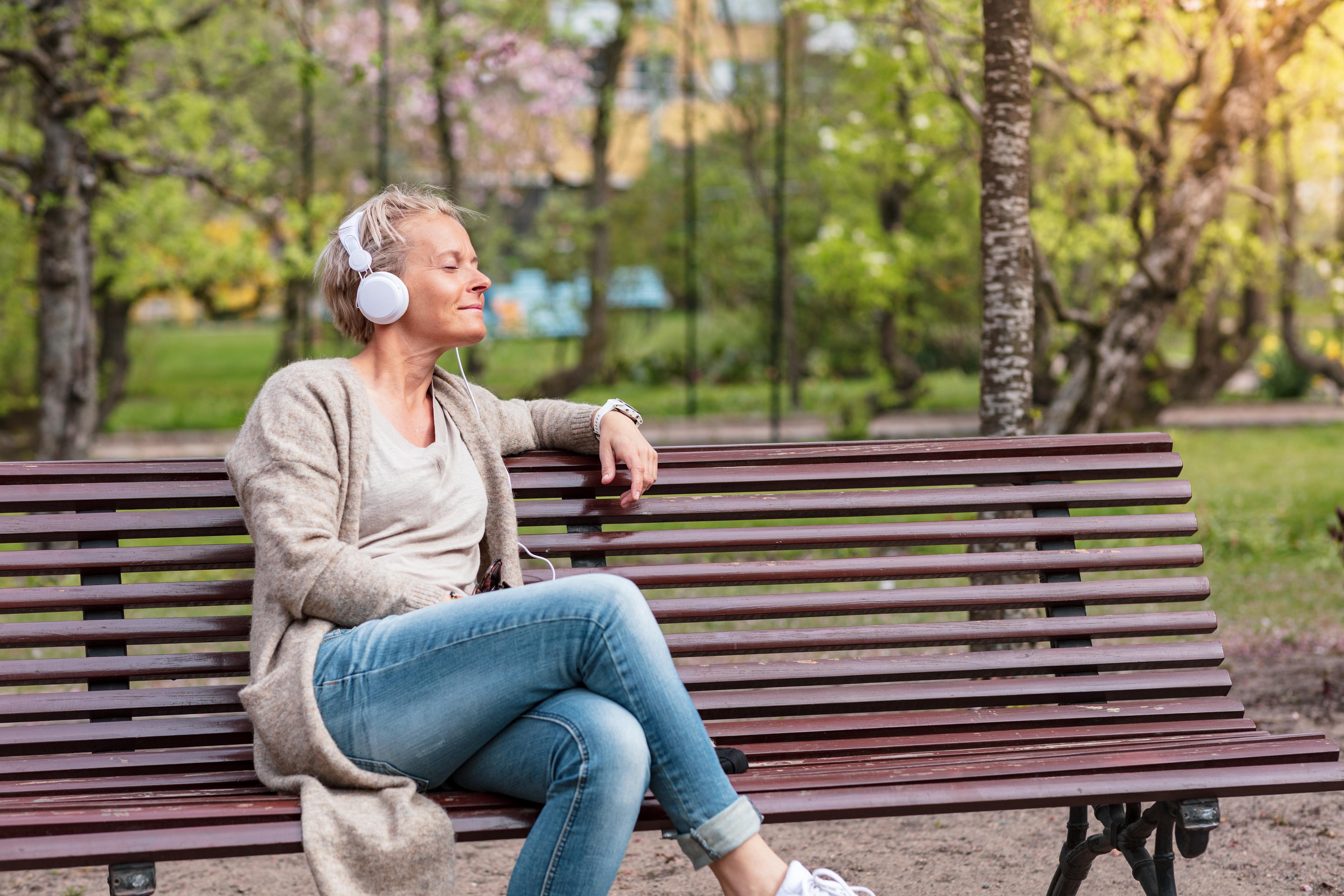 En kvinna sitter på en bänk och lyssnar på musik